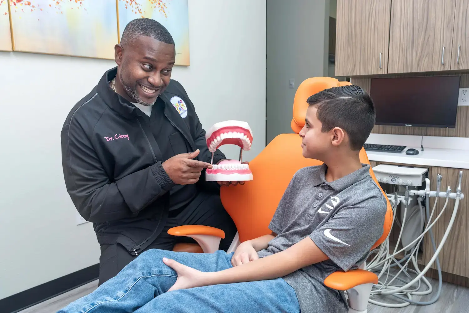 Dr. Jerry Chery showing a dental model to a young patient in the exam chair